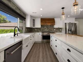 Experience modern luxury in this stunning kitchen, featuring sleek white cabinetry, a farmhouse sink, and a striking wood range hood.