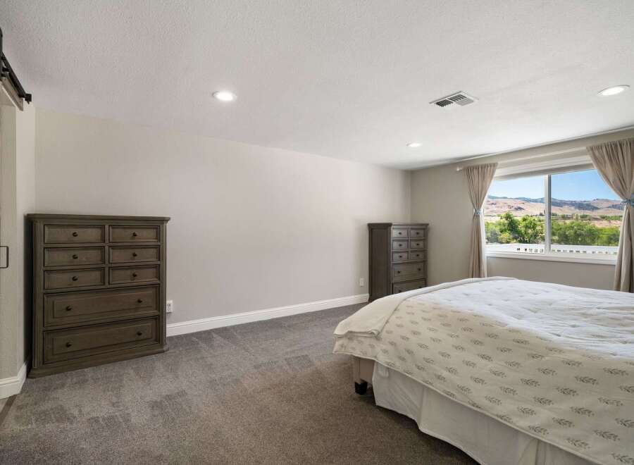 This spacious bedroom features a large window with scenic views of rolling hills and lush greenery, perfect for enjoying natural light and picturesque sunsets.
