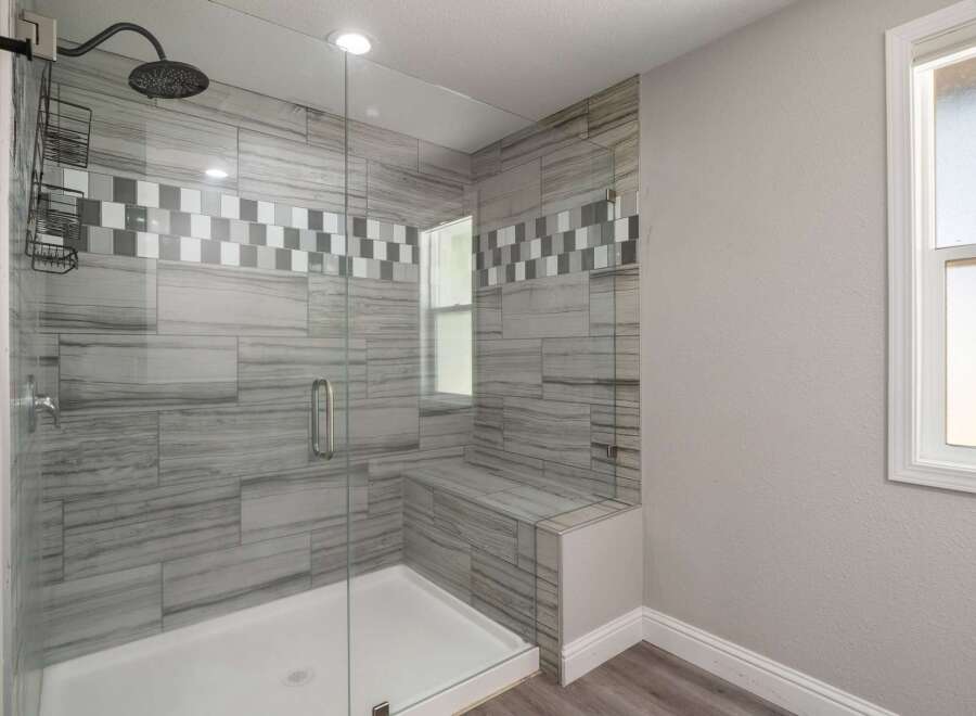 Experience luxury in this modern bathroom featuring a spacious walk-in shower with elegant gray wood-look tile and a decorative mosaic accent.