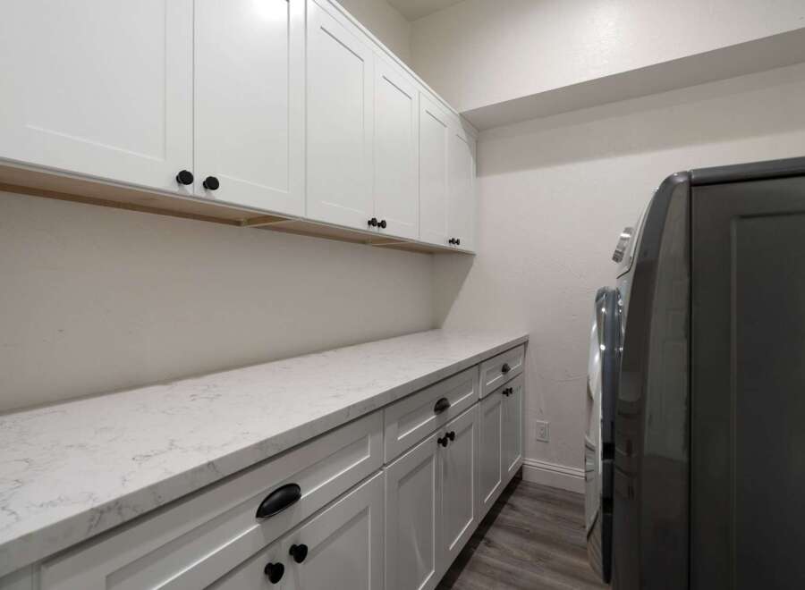 This laundry room features ample white cabinetry, including upper cabinets and a long countertop with lower cabinets, providing abundant storage and workspace.