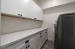 This laundry room features ample white cabinetry, including upper cabinets and a long countertop with lower cabinets, providing abundant storage and workspace.
