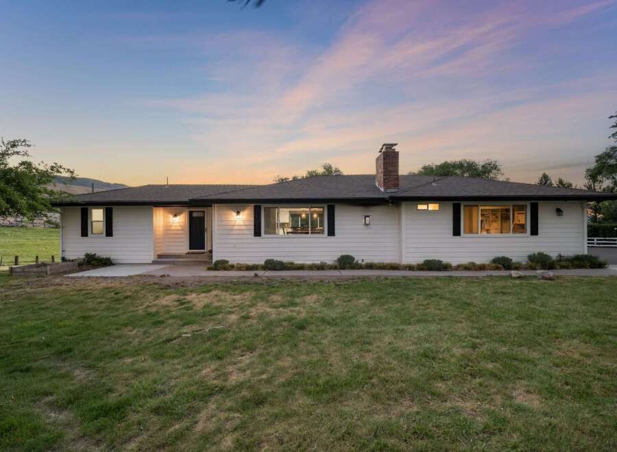 Experience serene living in this charming white ranch-style home, nestled against a backdrop of rolling hills and a picturesque sunset.