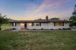 Experience serene living in this charming white ranch-style home, nestled against a backdrop of rolling hills and a picturesque sunset.
