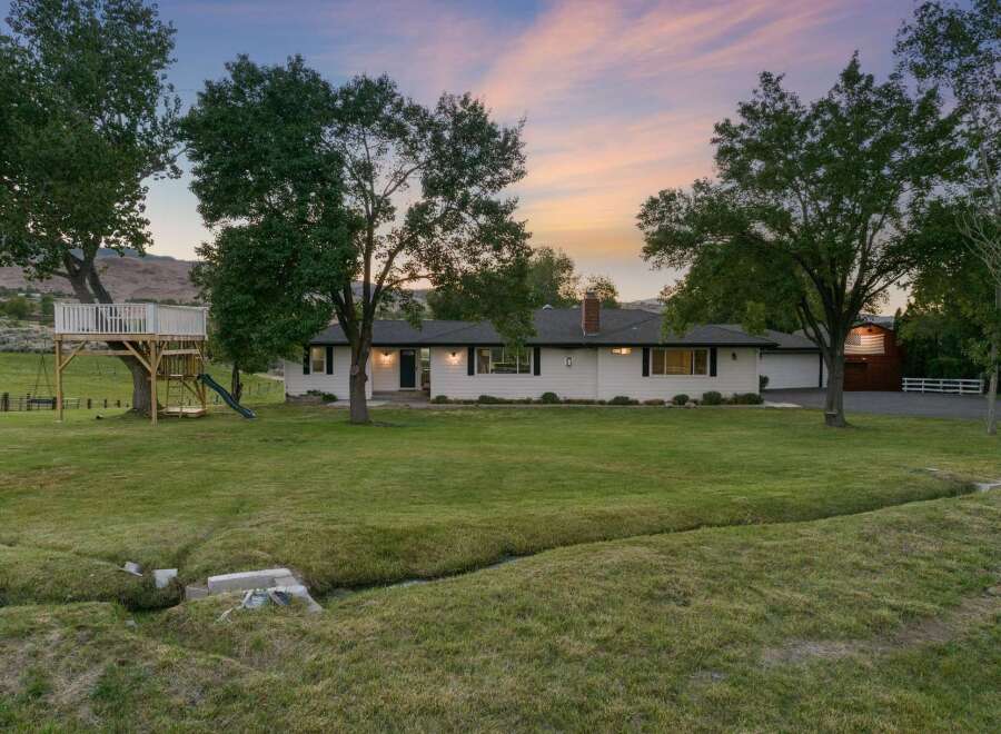 Discover this charming white ranch-style home nestled on a sprawling green lawn, perfect for outdoor enjoyment.