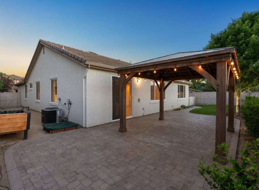 Enjoy outdoor living with this charming backyard featuring a spacious paver patio and a covered wooden pergola adorned with string lights.
