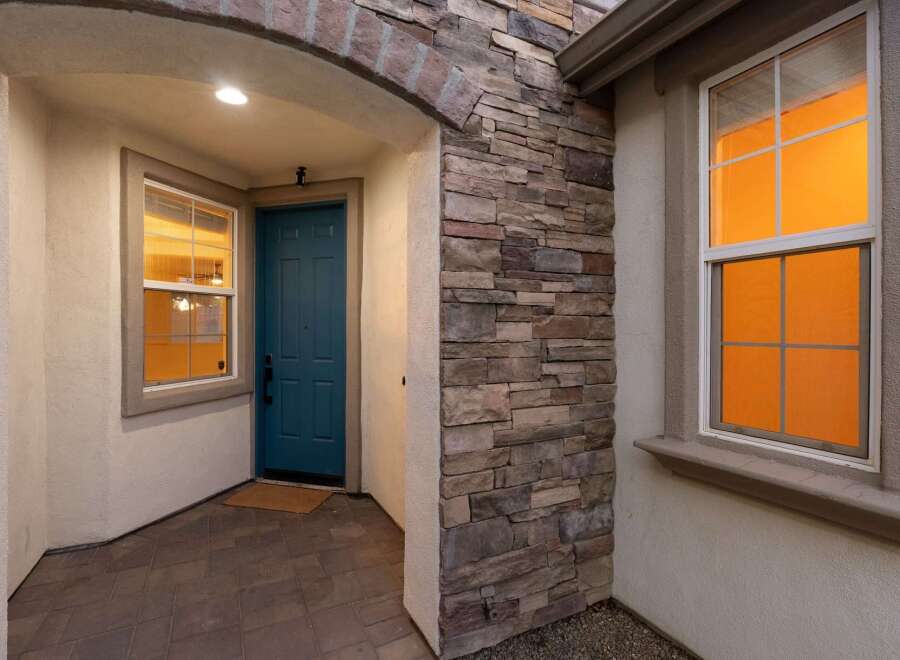 Welcome guests into this charming home through a covered entryway featuring a vibrant teal front door and a welcoming stone accent wall.