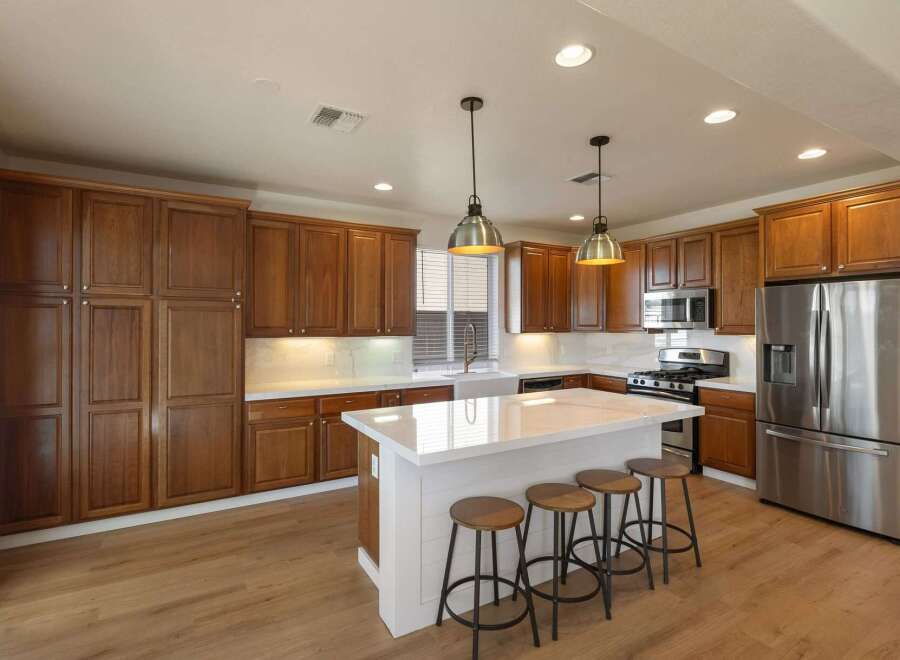 This stunning kitchen boasts rich wood cabinetry, complemented by sleek white countertops and a modern island with bar seating.