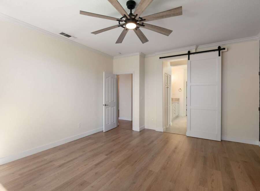 Experience modern living in this spacious bedroom featuring elegant wood-look flooring and a stylish ceiling fan.
