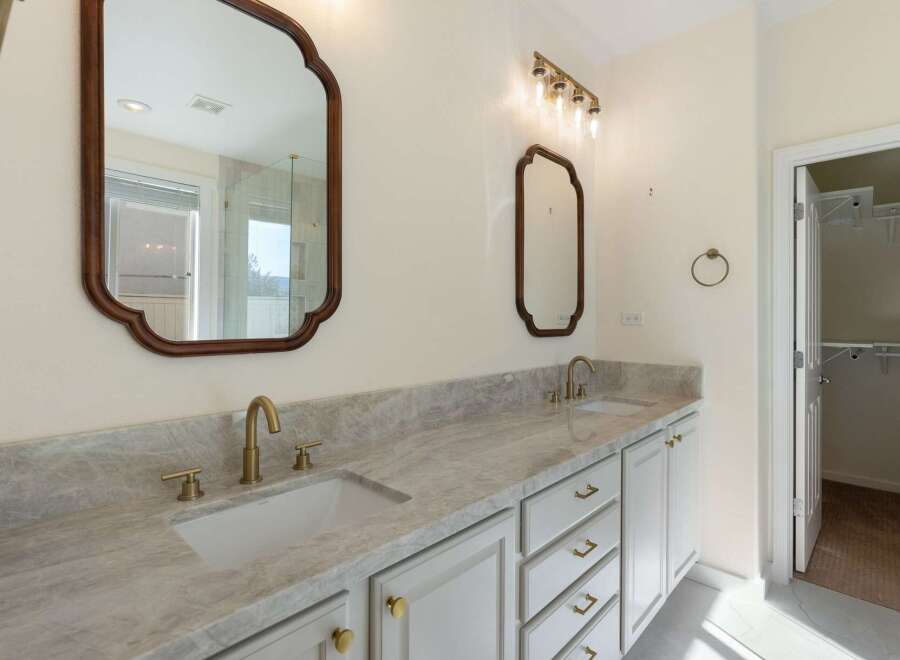 This elegant bathroom features a spacious double vanity with a stunning marble countertop and modern brass fixtures.