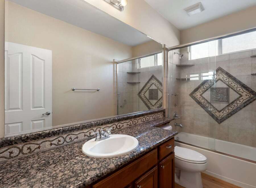 This bathroom features a granite countertop with an ornate mosaic tile backsplash, complemented by a white undermount sink and chrome fixtures.