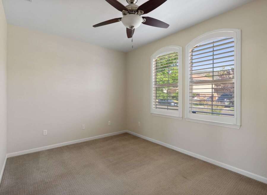 Discover comfort and style in this inviting bedroom, featuring a ceiling fan for optimal air circulation and large arched windows that flood the space with natural light.