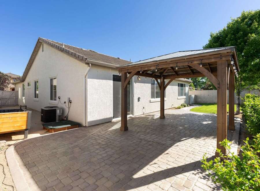 Enjoy outdoor living with this charming backyard featuring a spacious paver patio and a rustic wooden pergola adorned with string lights.