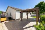 Enjoy outdoor living with this charming backyard featuring a spacious paver patio and a rustic wooden pergola adorned with string lights.