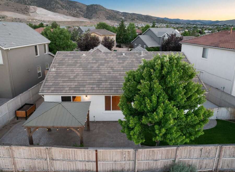 Enjoy outdoor living in this backyard featuring a paved patio, a covered gazebo with string lights, and a wooden planter box.