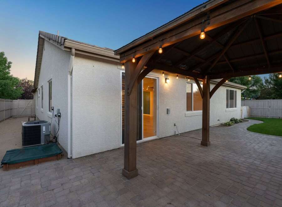 Enjoy outdoor living with this charming backyard featuring a spacious paver patio and a covered wooden pergola adorned with string lights.