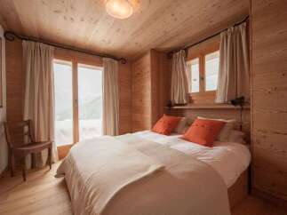 Experience cozy mountain living in this charming wooden bedroom, featuring large windows with stunning snowy views.
