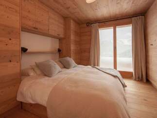 Experience cozy mountain living in this charming bedroom, featuring warm wood paneling throughout and a comfortable bed adorned with plush pillows.