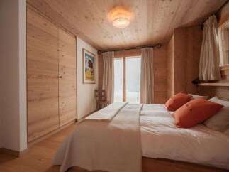 Experience cozy mountain living in this charming bedroom, featuring warm wood paneling throughout and a comfortable bed adorned with vibrant orange accent pillows.