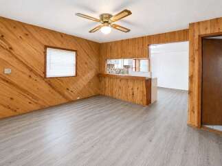 Step into this charming living space featuring warm wood-paneled walls and a convenient breakfast bar overlooking the kitchen.