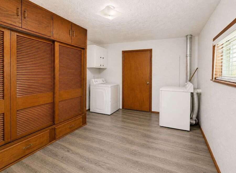 Discover ample storage with this spacious laundry room, featuring a large wooden cabinet with louvered doors and built-in drawers.