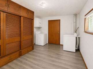 Discover ample storage with this spacious laundry room, featuring a large wooden cabinet with louvered doors and built-in drawers.