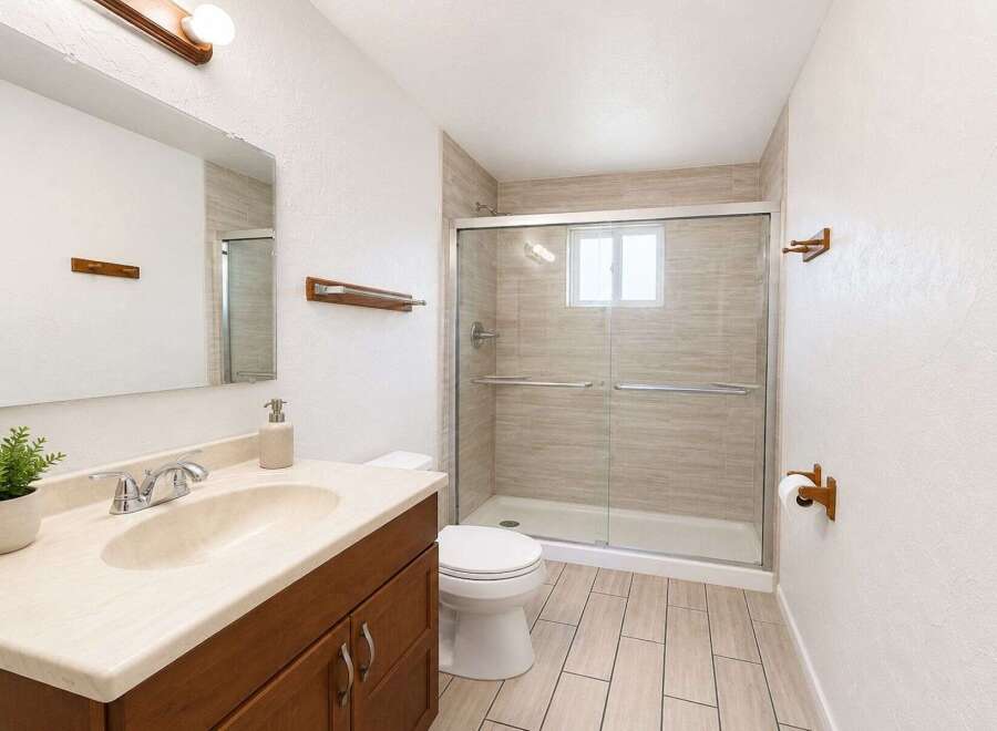 This modern bathroom features a sleek vanity with a cream countertop and a dark wood cabinet, complemented by a large mirror and a decorative plant.