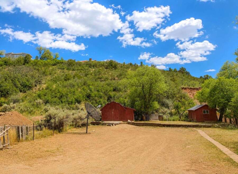 Discover this unique property featuring rustic red barns nestled against a lush, green hillside under a vibrant blue sky with fluffy white clouds.