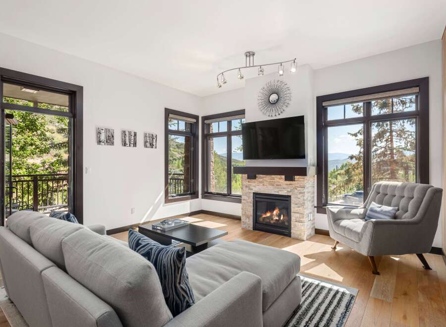 Experience breathtaking mountain views from this stunning living room, featuring a cozy stone fireplace and a large sectional sofa perfect for relaxation.