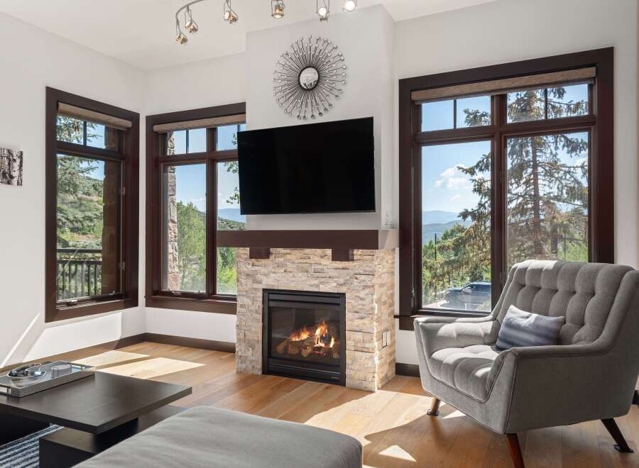Experience breathtaking mountain views from this stunning living room, featuring a cozy stone fireplace and a large flat-screen TV.