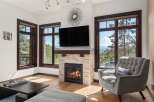 Experience breathtaking mountain views from this stunning living room, featuring a cozy stone fireplace and a large flat-screen TV.