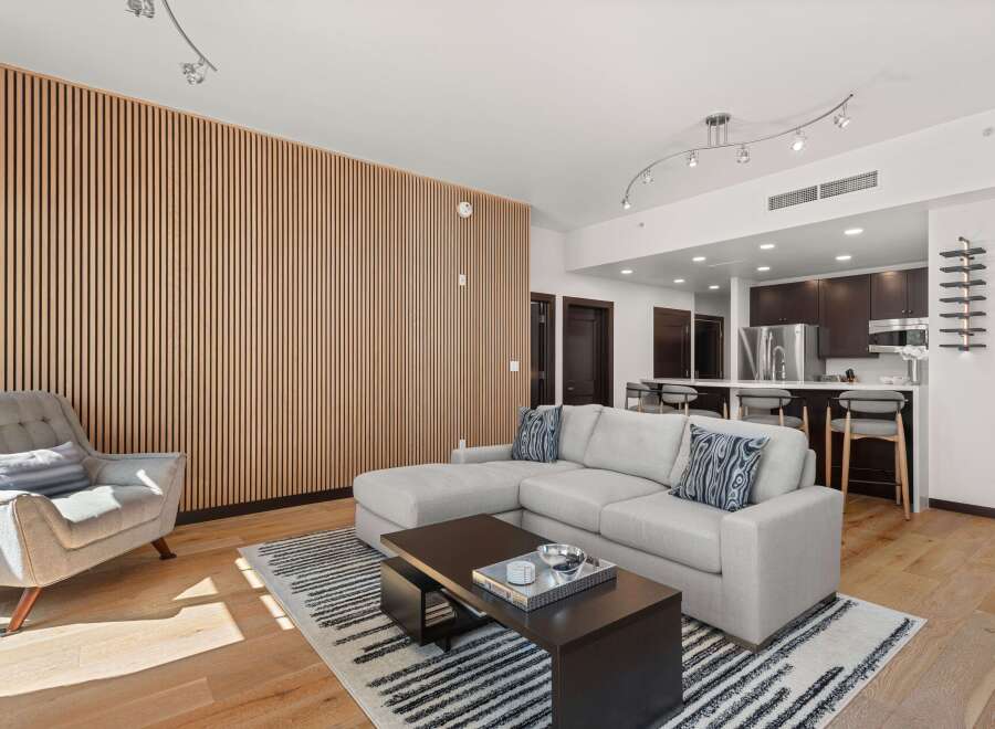 Experience modern living in this open-concept space featuring a stylish sectional sofa and a unique slatted wood accent wall.