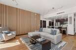 Experience modern living in this open-concept space featuring a stylish sectional sofa and a unique slatted wood accent wall.