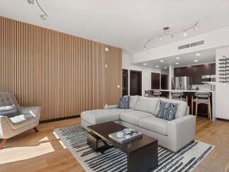 Experience modern living in this open-concept space featuring a stylish sectional sofa and a unique slatted wood accent wall.