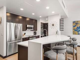 Experience modern living in this stunning kitchen, featuring sleek dark wood cabinetry and a spacious white quartz island perfect for entertaining.