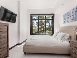 Experience serene mountain living in this beautifully appointed bedroom, featuring a plush bed and a large window with stunning tree-lined views.