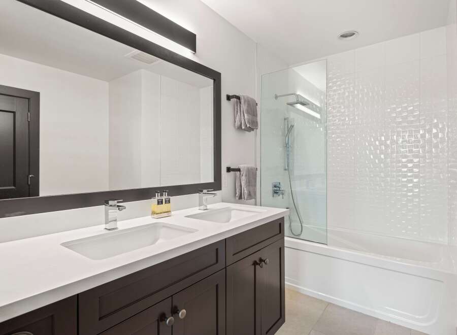 This modern bathroom features a sleek double vanity with chrome faucets and a large, dark-framed mirror.