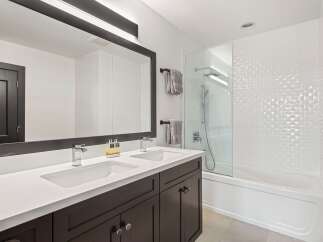 This modern bathroom features a sleek double vanity with chrome faucets and a large, dark-framed mirror.