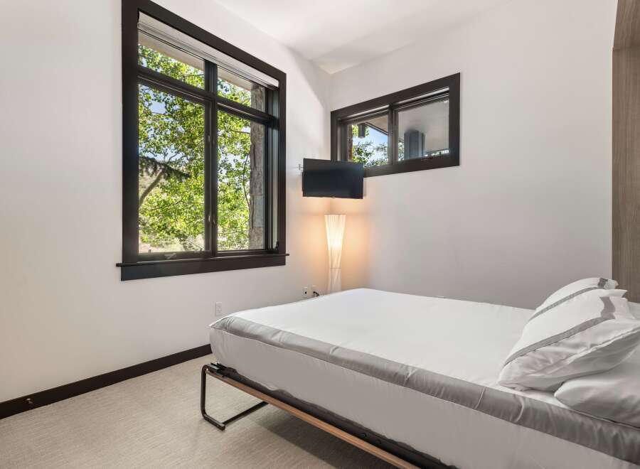 Experience serene living in this modern bedroom, featuring a comfortable bed adorned with crisp white linens and elegant grey trim.