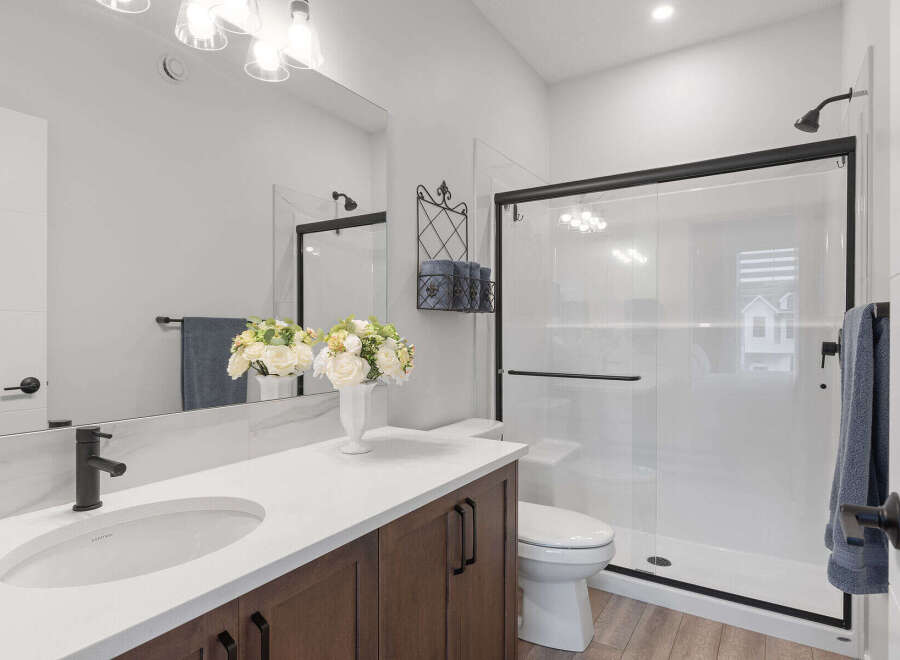 This modern bathroom features a sleek vanity with a white countertop and dark wood cabinets, complemented by a stylish black faucet.