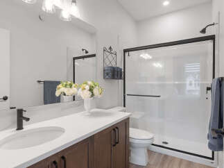 This modern bathroom features a sleek vanity with a white countertop and dark wood cabinets, complemented by a stylish black faucet.