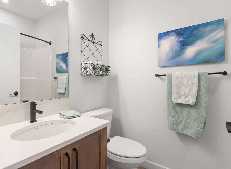 This modern bathroom features a sleek vanity with a white countertop and dark wood cabinets, complemented by a black faucet and a large mirror.