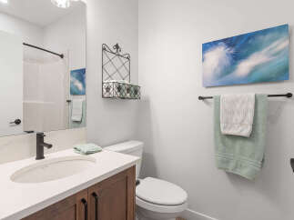 This modern bathroom features a sleek vanity with a white countertop and dark wood cabinets, complemented by a black faucet and a large mirror.