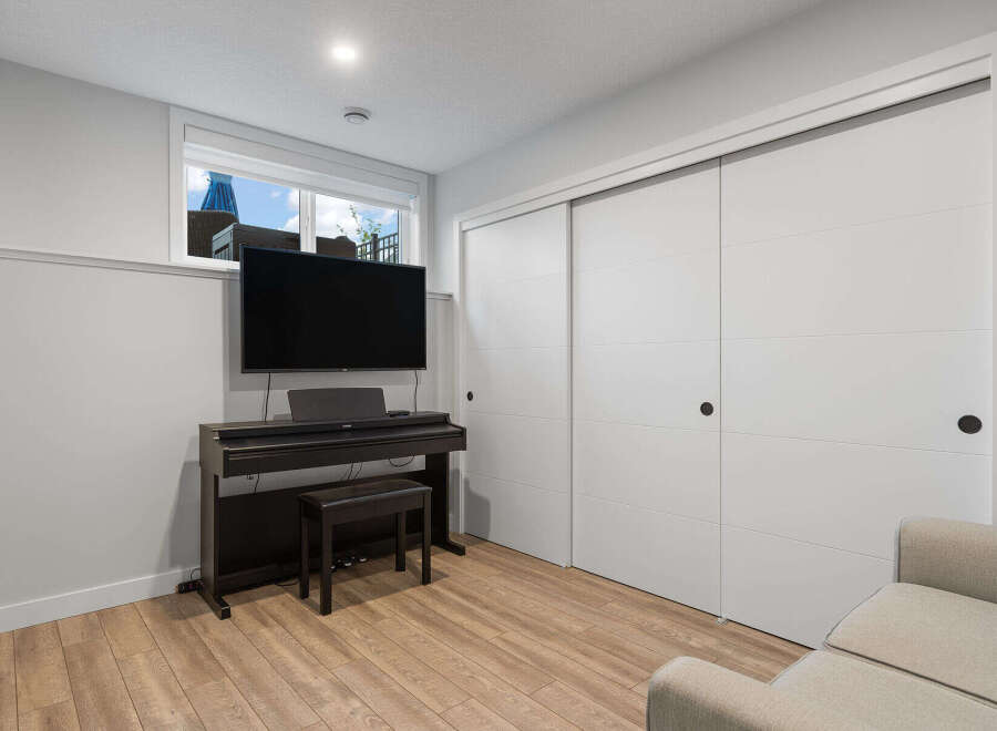 This modern living space features a sleek entertainment setup with a large flat-screen TV mounted above a digital piano and bench.