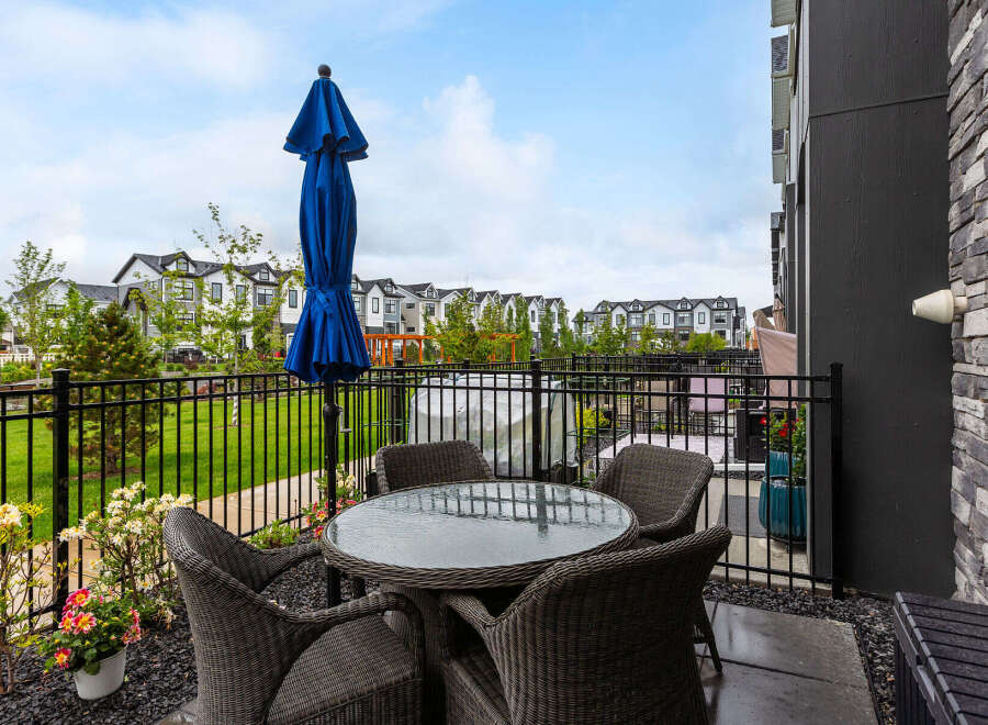 Enjoy outdoor living on this charming patio featuring a glass-top dining table with four wicker chairs and a vibrant blue umbrella.