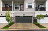 Discover modern living in this townhouse featuring a sleek dark gray garage door and a charming balcony with decorative screening.