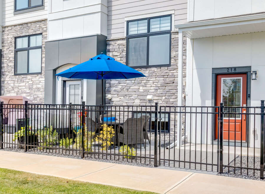 Enjoy outdoor living with this charming patio featuring a vibrant blue umbrella and comfortable seating, perfect for relaxing or entertaining.