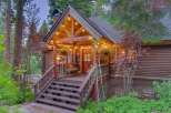 Charming log cabin nestled amongst tall trees, featuring a welcoming porch with string lights and a cozy seating area.