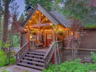 Charming log cabin nestled amongst tall trees, featuring a welcoming porch with string lights and a cozy seating area.