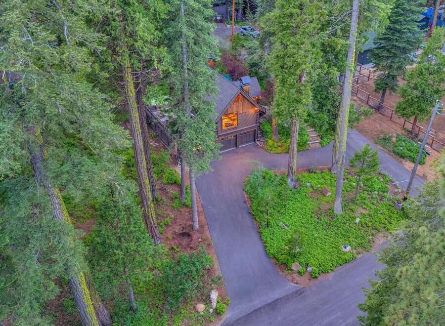 Nestled amidst towering trees, this stunning property offers a secluded retreat with a charming wooden home featuring a prominent gable window and a spacious attached garage.