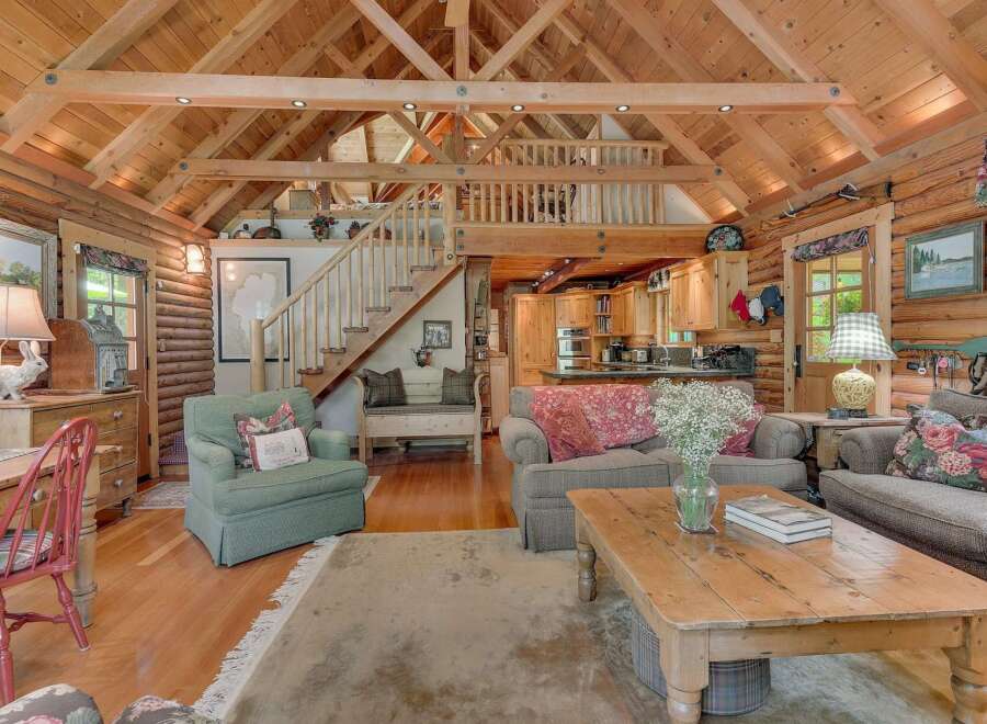 Experience rustic charm in this stunning log cabin living space, featuring a soaring vaulted ceiling with exposed wooden beams and a cozy loft overlooking the main area.